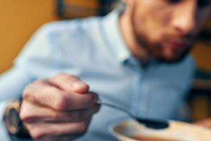un hermoso hombre con un barba come sopa de remolacha en un plato a un mesa en un café y un reloj en su mano foto