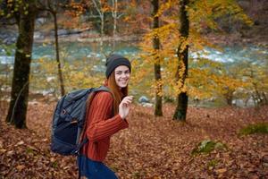 mujer en un suéter con un mochila en su espalda cerca el río en el montañas y parque arboles otoño paisaje foto