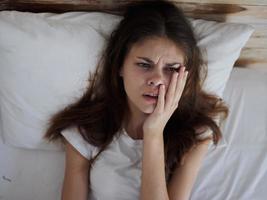 sick woman lying in bed hand on face discontent photo
