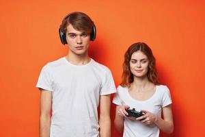 young couple in white t-shirts with joysticks playing a console orange background photo