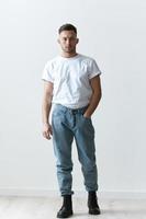 Full body shot of handsome serious tanned man guy in basic t-shirt holds hand on jeans posing on white background. Fashion Style New Collection Offer. Copy space for ad. Modeling snapshots photo