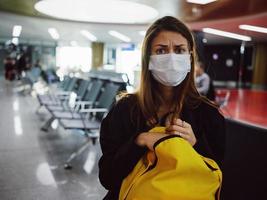 woman with displeased facial expression medical mask yellow backpack waiting airport photo