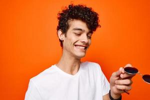 guy with curly hair sunglasses in hands cropped view orange background photo