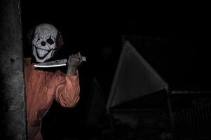 Asian handsome man wear clown mask with weapon at the night scene,Halloween festival concept,Horror scary photo of a killer in orange cloth
