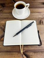 Coffee in a cup and a notebook with a pen. Vertical photo. photo