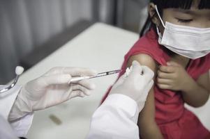 asiático médico inyección vacuna para proteger virus covid-19 a un niña vestir médico máscara, gente son muchachas son vacunado en contra influenza cada año. foto