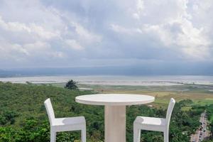 Empty white chair and table with beautiful background and cloudy sky. The photo is suitable to use for traditional food background, poster and food content media.