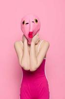 mujer en un pescado disfraz para Víspera de Todos los Santos poses en contra un rosado antecedentes en un loco de miedo disfraz con un rosado silicona máscara en su cabeza foto
