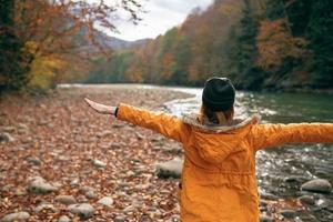 mujer lanza arriba su manos en naturaleza otoño bosque río caído hojas foto
