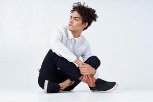 young man with curly hair sits cross-legged on the floor photo