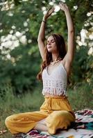 A young hippie woman meditates in nature in the park, sitting in a lotus position on her colorful plaid and enjoying harmony with the world in eco-clothing in the autumn photo