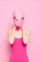 Woman standing in a pink fish mask on her head, a provocative crazy Halloween look, pink background in the studio photo