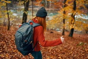 woman hiker with backpack in autumn forest near mountain river and fallen leaves photo