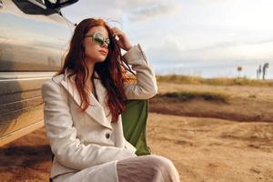 bonito mujer sentado en un silla en un campo vistiendo oscuro lentes cerca el coche soleado día foto