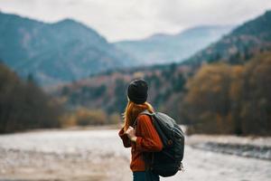 woman in a hat with a backpack are resting in the mountains in nature near the river photo