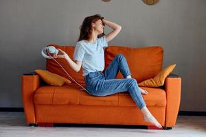 sonriente mujer en el naranja sofá escuchando a música con auriculares tecnologías foto