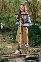 A woman farmer in work clothes and an apron works outdoors in nature and holds a rake to gather grass photo