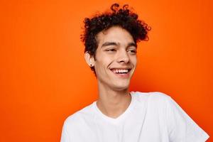 young guy in white t-shirt curly hair smile orange background photo