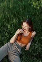 The view from above is a woman lying on the green grass in the park and relaxing in nature smiling and enjoying life. The concept of a healthy lifestyle photo
