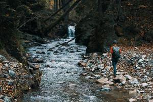 mujer turista con un mochila caminado a lo largo el banco cerca el río, un corriente de agua y alto arboles foto