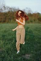 A woman works out and runs through the field in the park with a smile in a good mood looking at the beautiful summer nature around her photo