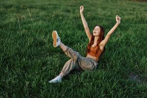A woman lies on the green grass in the park with her legs up and having fun against the lawn, viewed from above. The concept of relaxing in nature and caring for the environment photo
