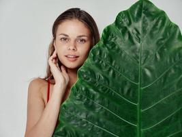 young woman in a red t-shirt with a green leaf of a palm tree on a light background photo