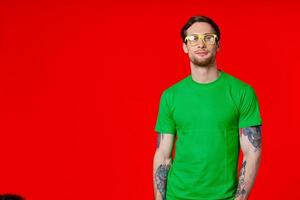 a man in a green t-shirt with tattoos in his hands wearing glasses on a red background photo