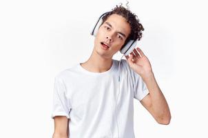 happy curly-haired guy in headphones and in a white t-shirt listens to music and holds his hands near his face photo