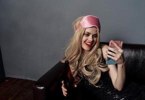 A drunk woman on the couch is taking pictures of herself on a cell phone photo