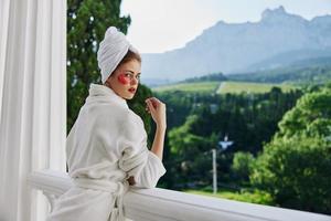 a fit girl in a white robe the balcony overlooks the mountains looking on the view photo