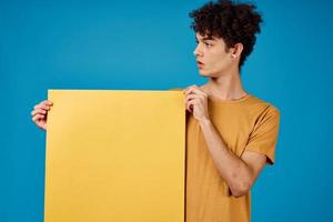 Cheerful man with curly hair yellow poster advertising blue background photo