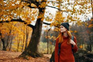 mujer en un suéter camina en el parque en otoño naturaleza paisaje Fresco aire modelo mochila foto