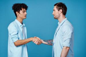 curly guy in a shirt stands next to a young man in a t-shirt on a blue background cropped view photo