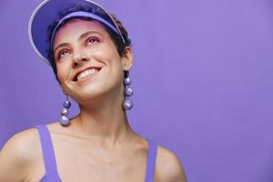 retrato de un deportivo Moda mujer posando sonriente en un púrpura Deportes traje para yoga y un transparente gorra en un púrpura antecedentes monocromo foto