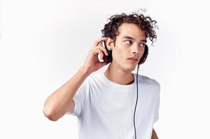 emotional guy with curly hair in headphones listens to music on a light background photo