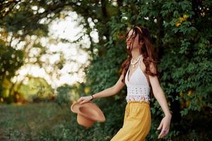 A woman in eco-friendly clothing in a hippie look dances in nature in the park and smiles at the world. The concept of harmony with the body and the surrounding nature photo