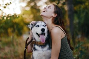 un mujer con un fornido raza perro sonrisas y afectuosamente golpes su amado perro mientras caminando en naturaleza en el parque en otoño en contra el fondo de puesta de sol foto