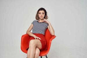 hermosa mujer en un a rayas camiseta sentado en el rojo silla moderno estilo peinado foto