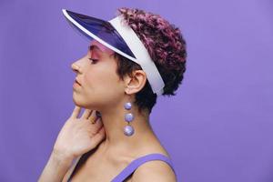 retrato de un deportivo Moda mujer posando sonriente en un púrpura Deportes traje para yoga y un transparente gorra en un púrpura antecedentes monocromo foto