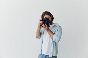 A male hipster photographer in a studio against a white background looks through the camera viewfinder and shoots shots with natural light from the window. Lifestyle work as a freelance photographer photo