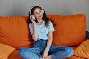 woman listening to music with headphones on the orange sofa unaltered photo