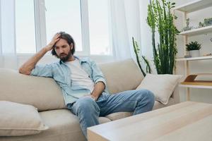 A young male freelancer sits on the couch after a demanding job and rests sadly leaning on the couch. photo