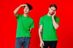 two friends in green t-shirts are standing next to tin with their hands emotions red background photo