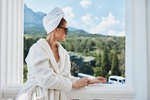 elegante mujer en un bata de baño en el Mañana en el balcón admirativo naturaleza montaña ver foto