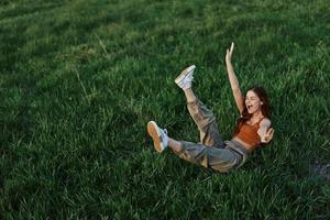 A young woman is playing in the park with us in the grass and falls to the ground smiling happily in the sunlight. Resting in nature, harmony with the body photo