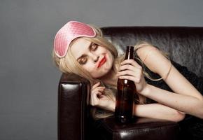 A woman with a pink mask on her head and a bottle of beer sleeps on the couch photo