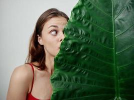 pretty woman in red swimsuit hiding behind green leaf emotion photo