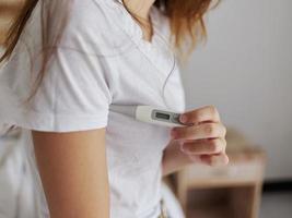 woman in white t-shirt hold thermometer armpit health temperature photo