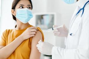 the patient in the hospital and the doctor in protective gloves inject the vaccine into the woman's shoulder photo